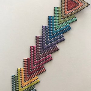 May include: A rainbow of colorful triangle-shaped beaded ornaments with black accents. The ornaments are arranged in a row, with the largest at the top and the smallest at the bottom. The ornaments are connected by a silver pin.