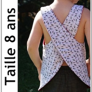 May include: A white sleeveless top with a floral pattern and a criss-cross back design. The top is labeled "Taille 8 ans".
