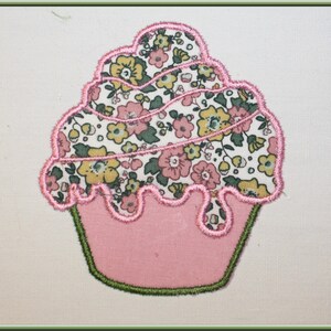 Peut inclure: Un cupcake rose avec un glaçage floral vert et blanc. Le cupcake est bordé de fil rose et vert.