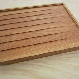 K&ouml;nnte beinhalten: Ein Holztablett mit hellbrauner Oberfl&auml;che und gerillter Oberfl&auml;che. Das Tablett hat einen erh&ouml;hten Rand um den Umfang.