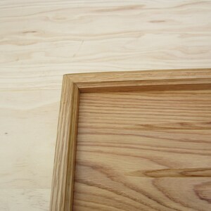 May include: A wooden tray with a natural wood finish. The tray has a raised edge and a smooth surface.