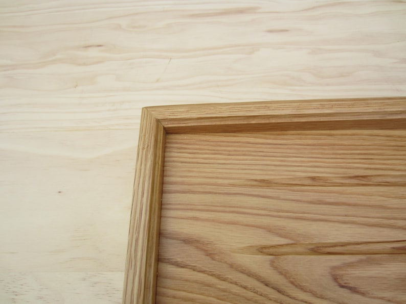 May include: A wooden tray with a natural wood finish. The tray has a raised edge and a smooth surface.