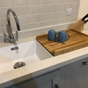 May include: A white kitchen sink with a chrome faucet and a wooden cutting board with two blue mugs on top. The cutting board is sitting on a gray countertop.