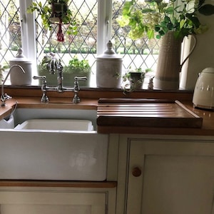 May include: A white porcelain farmhouse sink with a chrome double-handle faucet. The sink is installed in a kitchen with a wooden countertop and a white cabinet below. A cream-colored electric kettle is on the counter to the right of the sink.