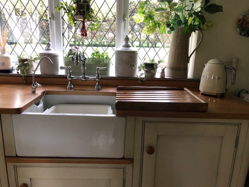 May include: A white porcelain farmhouse sink with a chrome double-handle faucet. The sink is installed in a kitchen with a wooden countertop and a white cabinet below. A cream-colored electric kettle is on the counter to the right of the sink.