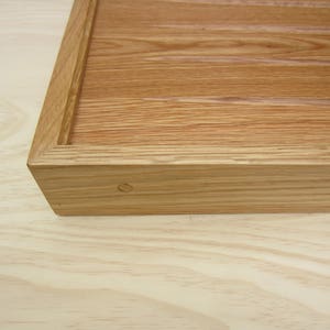 K&ouml;nnte beinhalten: Nahaufnahme einer Ecke eines Holztabletts mit nat&uuml;rlicher Holzmaserung. Das Tablett hat eine einfache, rechteckige Form und ist aus massivem Holz gefertigt.