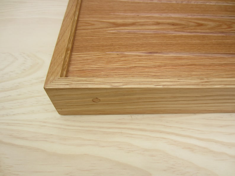 K&ouml;nnte beinhalten: Nahaufnahme einer Ecke eines Holztabletts mit nat&uuml;rlicher Holzmaserung. Das Tablett hat eine einfache, rechteckige Form und ist aus massivem Holz gefertigt.