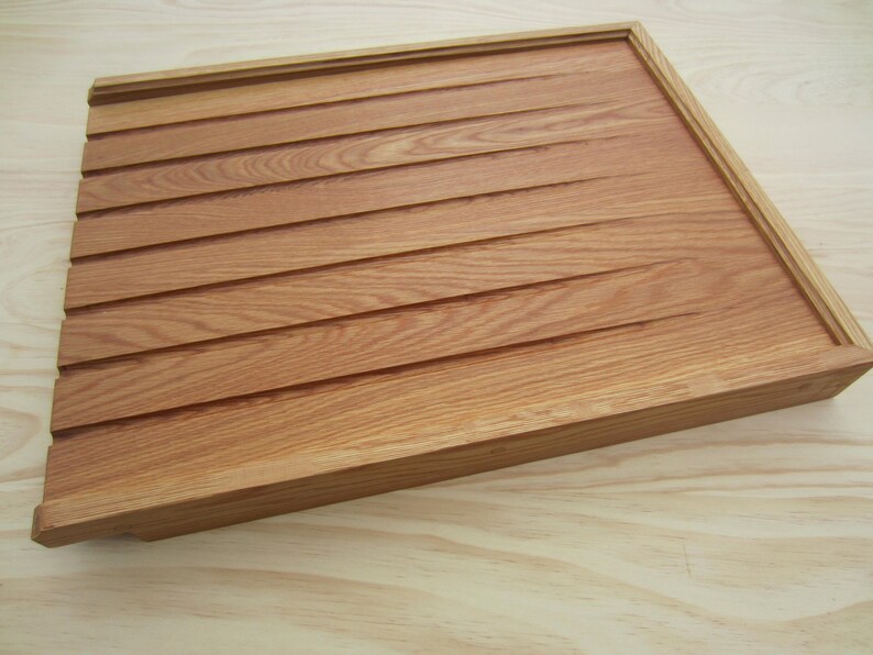 May include: A wooden tray with a light brown finish and a grooved surface. The tray has a raised edge and is made of solid wood.