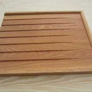 K&ouml;nnte beinhalten: Eine Holzplatte mit einer gerillten Oberfl&auml;che und einer hellbraunen Oberfl&auml;che. Die Platte hat einen einfachen Rahmen an den R&auml;ndern.