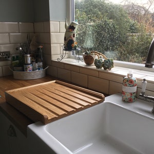 May include: A white porcelain kitchen sink with a wooden draining board. The sink has a chrome faucet and a bottle of soap with a floral design. The sink is set against a backdrop of white subway tiles.