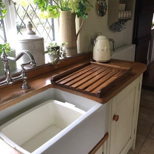 May include: A white porcelain farmhouse sink with a wooden draining board and a white electric kettle on the counter.
