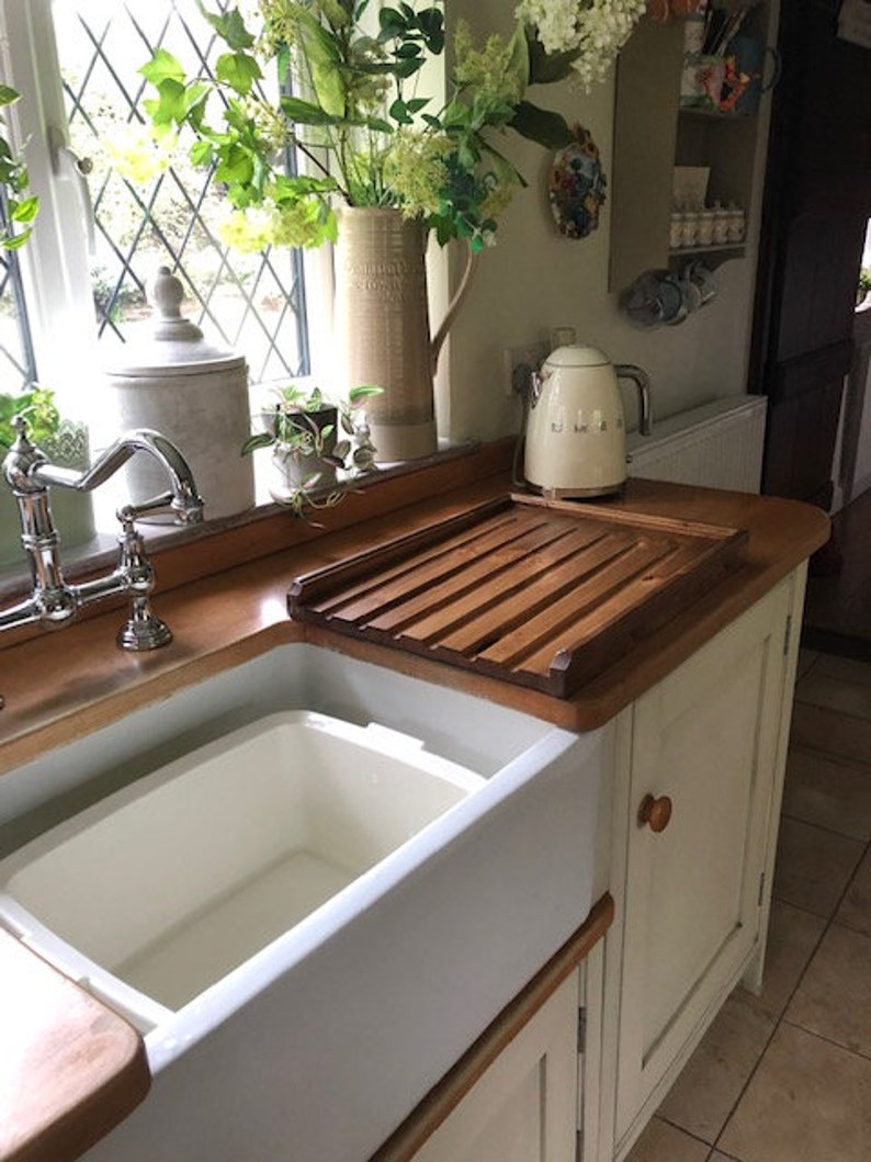 May include: A white porcelain farmhouse sink with a wooden draining board and a white electric kettle on the counter.