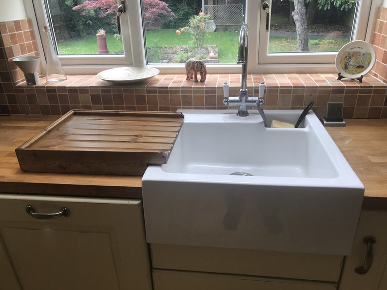 May include: A white porcelain kitchen sink with a chrome faucet and a wooden cutting board.