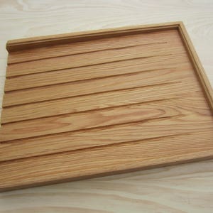 May include: A wooden tray with a grooved surface. The tray is made of light brown wood and has a rectangular shape.