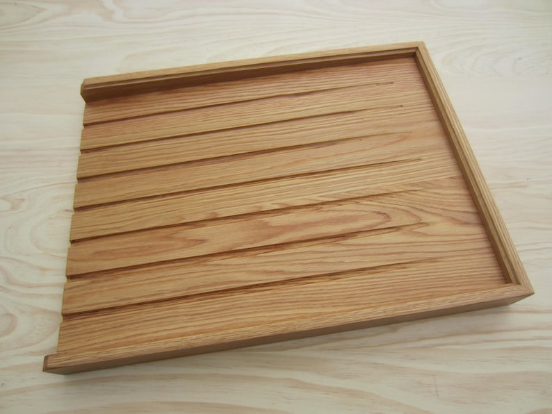 May include: A wooden tray with a grooved surface. The tray is made of light brown wood and has a rectangular shape.