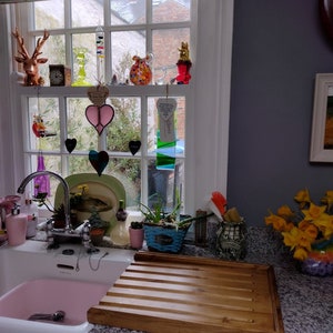 May include: A white porcelain kitchen sink with a pink basin. A wooden draining board with grooves sits on the counter next to the sink. A bouquet of yellow daffodils sits on the counter.