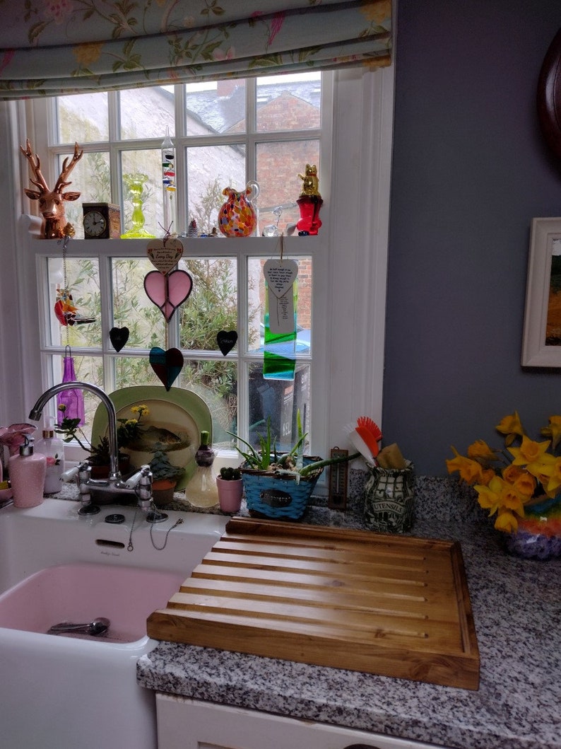 May include: A white porcelain kitchen sink with a pink basin. A wooden draining board with grooves sits on the counter next to the sink. A bouquet of yellow daffodils sits on the counter.