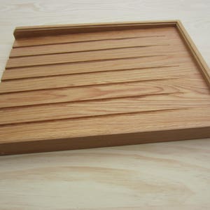 May include: A wooden tray with a grooved surface. The tray is made of light brown wood and has a rectangular shape.
