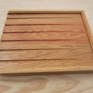 May include: A wooden tray with a grooved surface and a raised edge. The tray is made of light brown wood with a reddish hue.