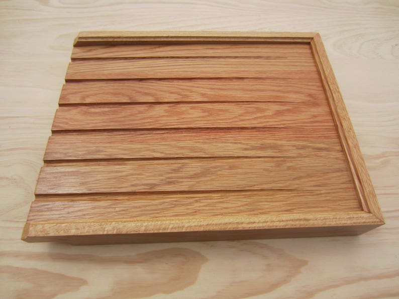 May include: A wooden tray with a grooved surface and a raised edge. The tray is made of light brown wood with a reddish hue.