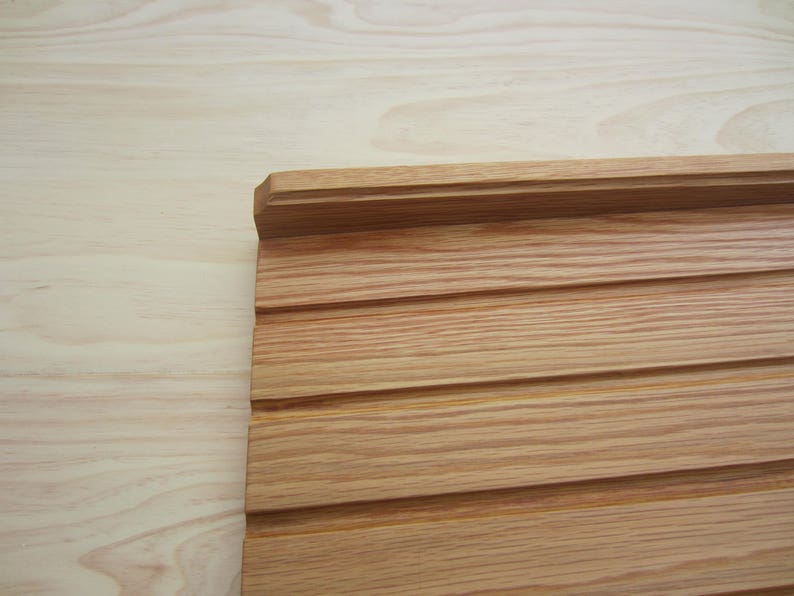 May include: A close-up of a light brown wood panel with a raised edge and horizontal grooves. The panel is made of natural wood with a smooth finish.