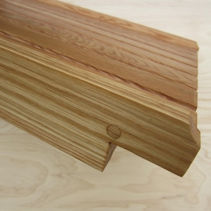 May include: A close-up of a wooden shelf with a natural wood finish. The shelf has a slightly curved edge and a small hole in the front. The shelf is made of multiple pieces of wood that are joined together.