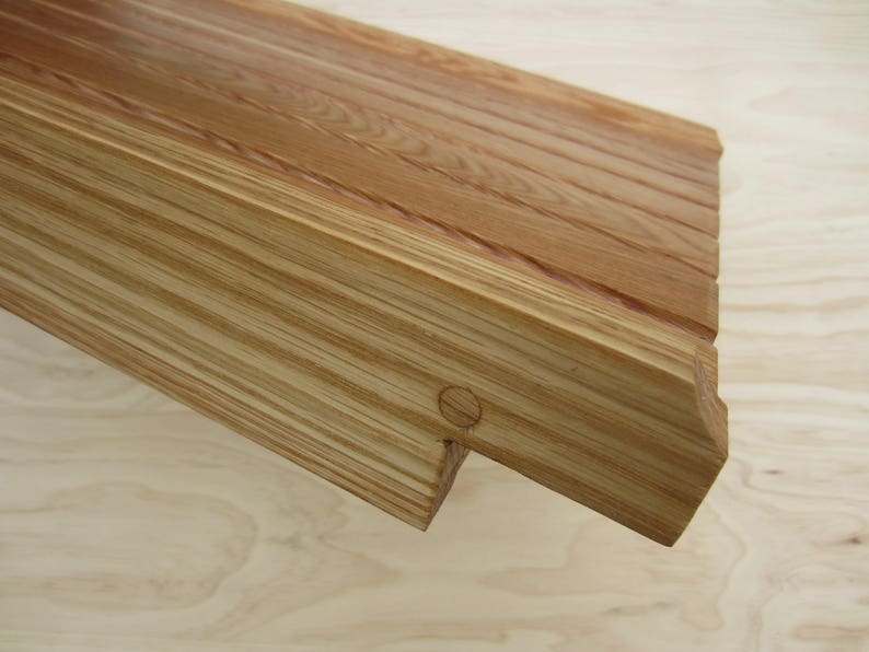 May include: A close-up of a wooden shelf with a natural wood finish. The shelf has a slightly curved edge and a small hole in the front. The shelf is made of multiple pieces of wood that are joined together.