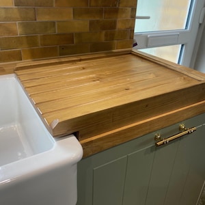 Könnte beinhalten: Ein hölzerner Spülbecken-Deckel aus hellem Holz liegt auf einem weißen Porzellanbecken. Das Becken ist in einen hellgrünen Schrank mit goldenen Griffen eingelassen. Die Rückwand besteht aus gelbbraunen Fliesen. Maße ca. 60 cm x 40 cm.