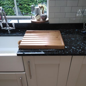 May include: A wooden cutting board with grooves sits on a black granite countertop in a kitchen. The countertop is next to a white kitchen cabinet with a silver handle.