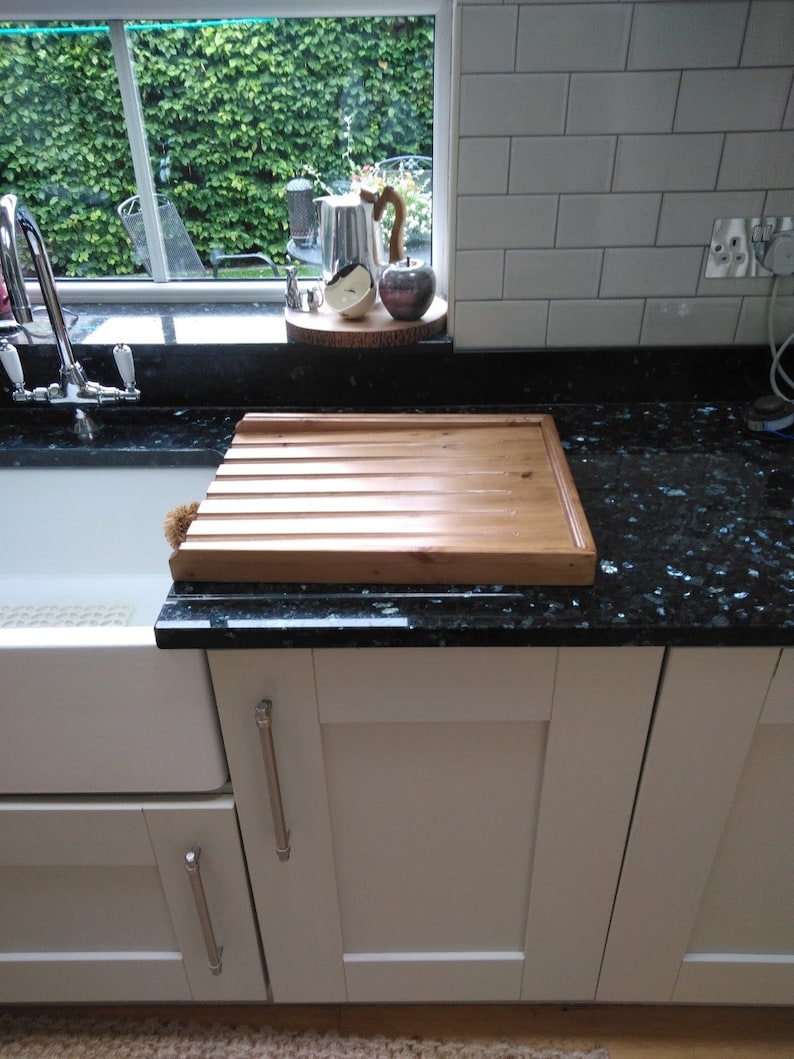 May include: A wooden cutting board with grooves sits on a black granite countertop in a kitchen. The countertop is next to a white kitchen cabinet with a silver handle.