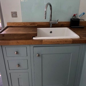 May include: A light blue kitchen cabinet with a white porcelain sink and a wooden cutting board. The cabinet has three drawers and a door with a silver knob.