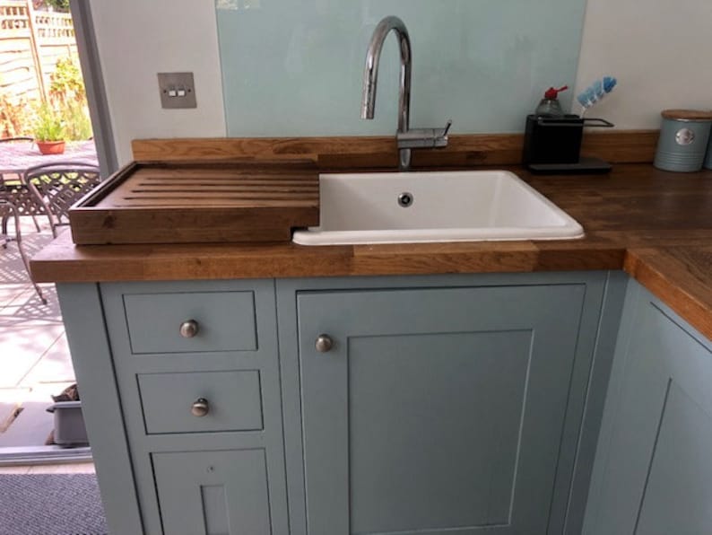 May include: A light blue kitchen cabinet with a white porcelain sink and a wooden cutting board. The cabinet has three drawers and a door with a silver knob.