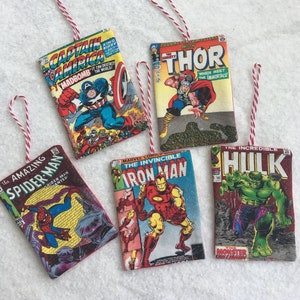 May include: Five vintage comic book ornaments featuring Marvel characters: Captain America, Thor, Spider-Man, Iron Man, and the Hulk. Each ornament is a replica of a comic book cover with a red and white string for hanging.