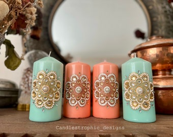 Könnte beinhalten: Vier dekorative Säulenkerzen in Mintgrün und Pfirsich. Jede Kerze hat ein aufwendiges Design mit Gold- und Silberverzierungen. Die Kerzen sind auf einer Holzoberfläche angeordnet, mit dem Text "Candlestrophic_designs" sichtbar.