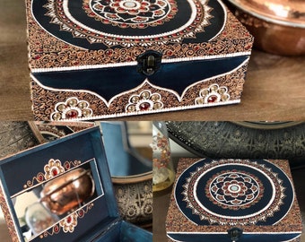 Könnte beinhalten: Eine dekorative Holzbox mit Scharnierdeckel, verziert mit aufwendigen Mandala-Mustern in Schwarz, Gold, Rot und Weiß. Die Box hat einen dunkelblauen Rand und ist mit dekorativen Edelsteinen verziert. Sie wird mit einem Metallverschluss verschlossen.