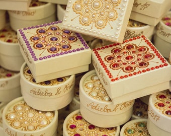 Könnte beinhalten: Eine Ansammlung cremefarbener dekorativer Schachteln, sowohl rund als auch quadratisch, verziert mit aufwendigen floralen Mustern. Die Schachteln sind mit Perlen und farbigen Edelsteinen verziert, was ihnen ein elegantes und festliches Aussehen verleiht. Einige Schachteln tragen den Text "Adieba & Onur" und das Datum "27-10-2017".