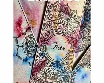 Könnte beinhalten: Aquarell-Lesezeichen mit aufwendigen schwarzen Mandala-Designs. Ein Lesezeichen zeigt den Namen "Ines" in einem zentralen Kreis. Der Hintergrund hat eine Aquarellwäsche aus Rosa, Blau und Gold. Das Wort "Example" steht oben.