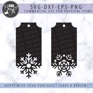 Op de afbeelding: Twee zwarte rechthoekige labels met witte sneeuwvlokontwerpen uitgesneden aan de onderkant. De labels hebben een gat aan de bovenkant om op te hangen. Tekst bovenaan zegt "SVG-DXF-EPS-PNG COMMERCIAL USE FOR PHYSICAL ITEMS".