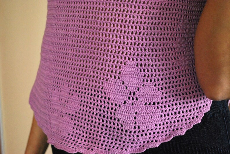 May include: A close-up of a pink crocheted top with a scalloped hem.