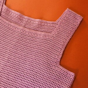 May include: A pink crocheted sleeveless top with a square neckline.