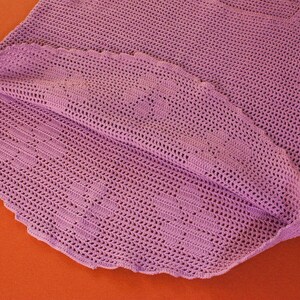 May include: A crocheted garment in a light purple color. The garment is made with a delicate stitch pattern and has a scalloped edge.
