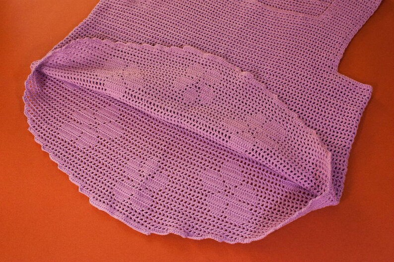 May include: A crocheted garment in a light purple color. The garment is made with a delicate stitch pattern and has a scalloped edge.