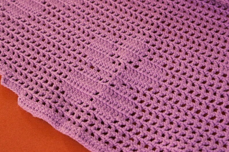May include: A close-up of a purple crocheted blanket with a diamond pattern.