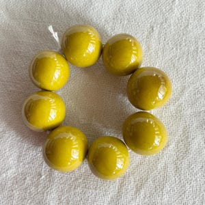 Peut inclure: Un bracelet circulaire composé de huit grosses perles sphériques et lisses avec une finition vert olive brillante. Les perles sont enfilées sur un fin cordon blanc, formant une boucle continue avec une texture de surface réfléchissante.