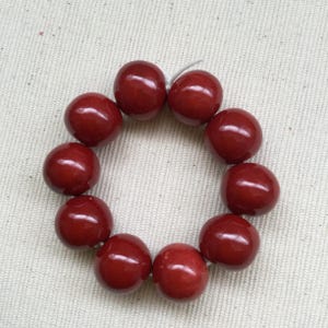 May include: A bracelet composed of ten large, round, glossy, dark red beads. The beads are strung together on a thin, white string, forming a circular shape. The beads have a smooth, polished surface, reflecting light.
