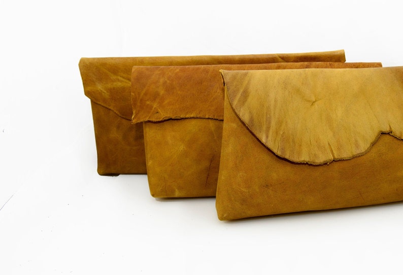 May include: Three brown leather clutches with a flap closure. The clutches are arranged in a row, with the largest clutch in the back and the smallest clutch in the front.