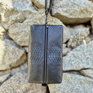 Peut inclure: Pochette zippée en cuir noir avec un motif peau de serpent.