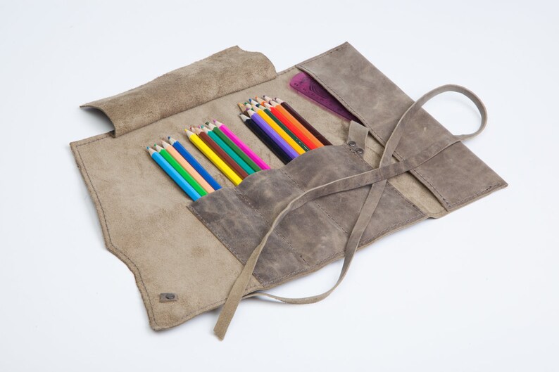 May include: A brown leather pencil roll with a strap closure. The roll is open and filled with colored pencils.