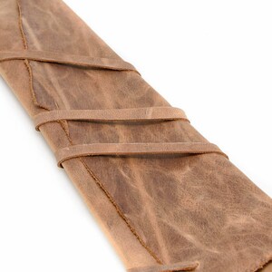 May include: A brown leather roll-up case with three straps to secure the contents. The case is made of distressed leather and has a rustic look.