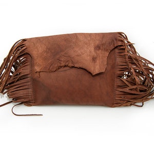 May include: A brown leather clutch bag with fringe detailing. The bag has a flap closure and a distressed look.